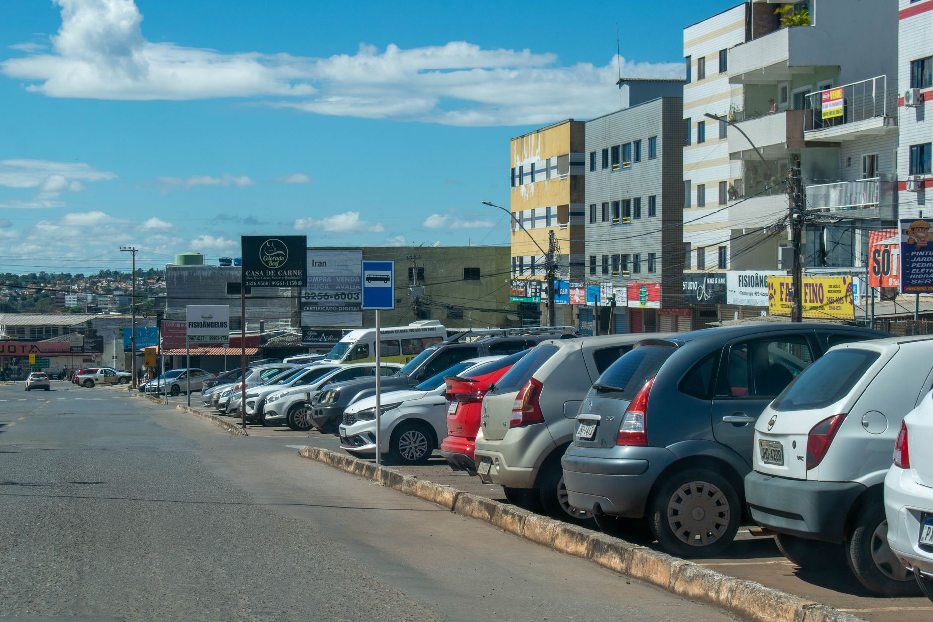 Carros estacionados ao longo de uma avenida com prédios ao fundo