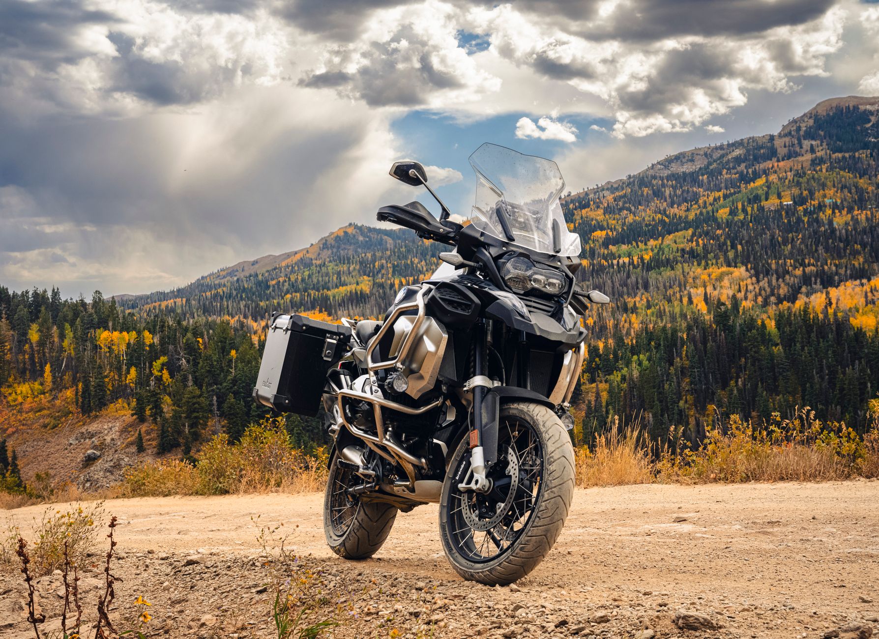 Moto de aventura parada em estrada de terra com montanhas e nuvens ao fundo
