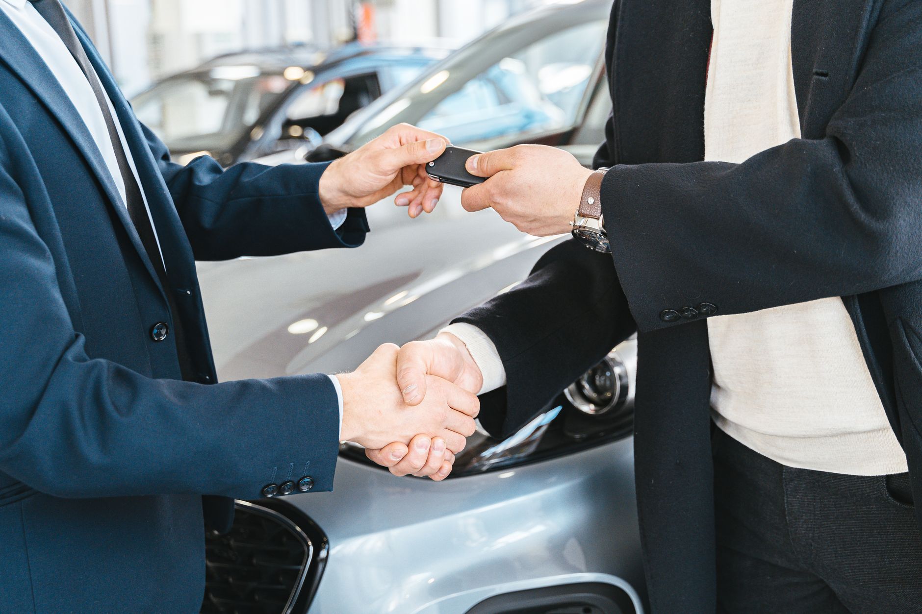 Aperto de mãos e entrega da chave entre vendedor e comprador ao lado de um carro