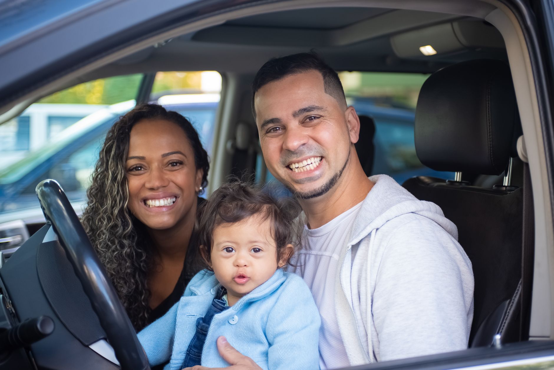 Casal com bebê sorrindo dentro de um carro novo