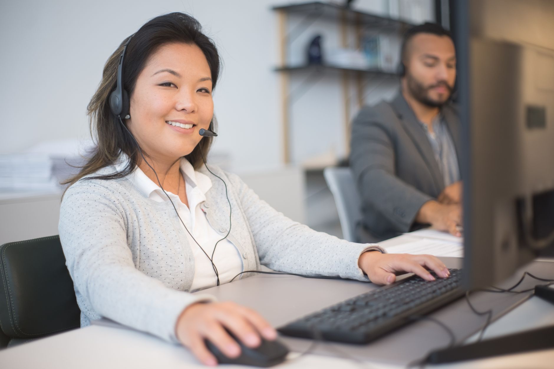 Atendente de suporte com fone de ouvido sorrindo diante do computador