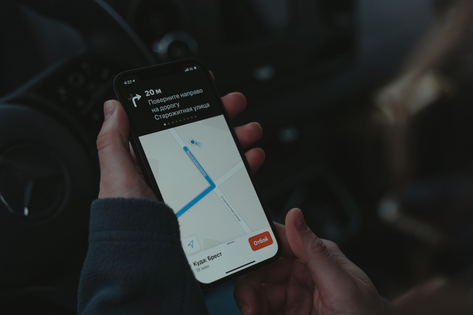Mão segurando celular com aplicativo de navegação aberto dentro do carro