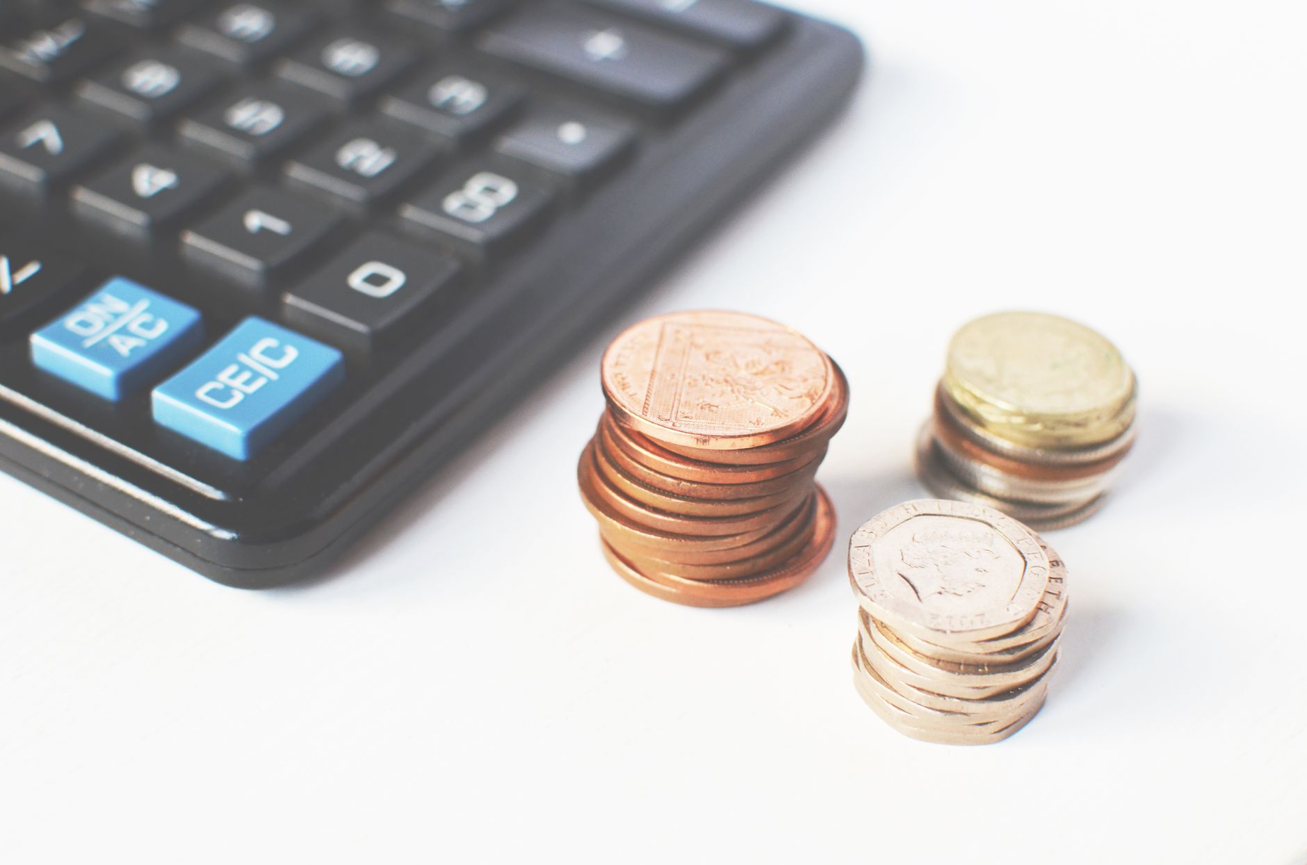 Calculadora e pilhas de moedas sobre uma mesa branca