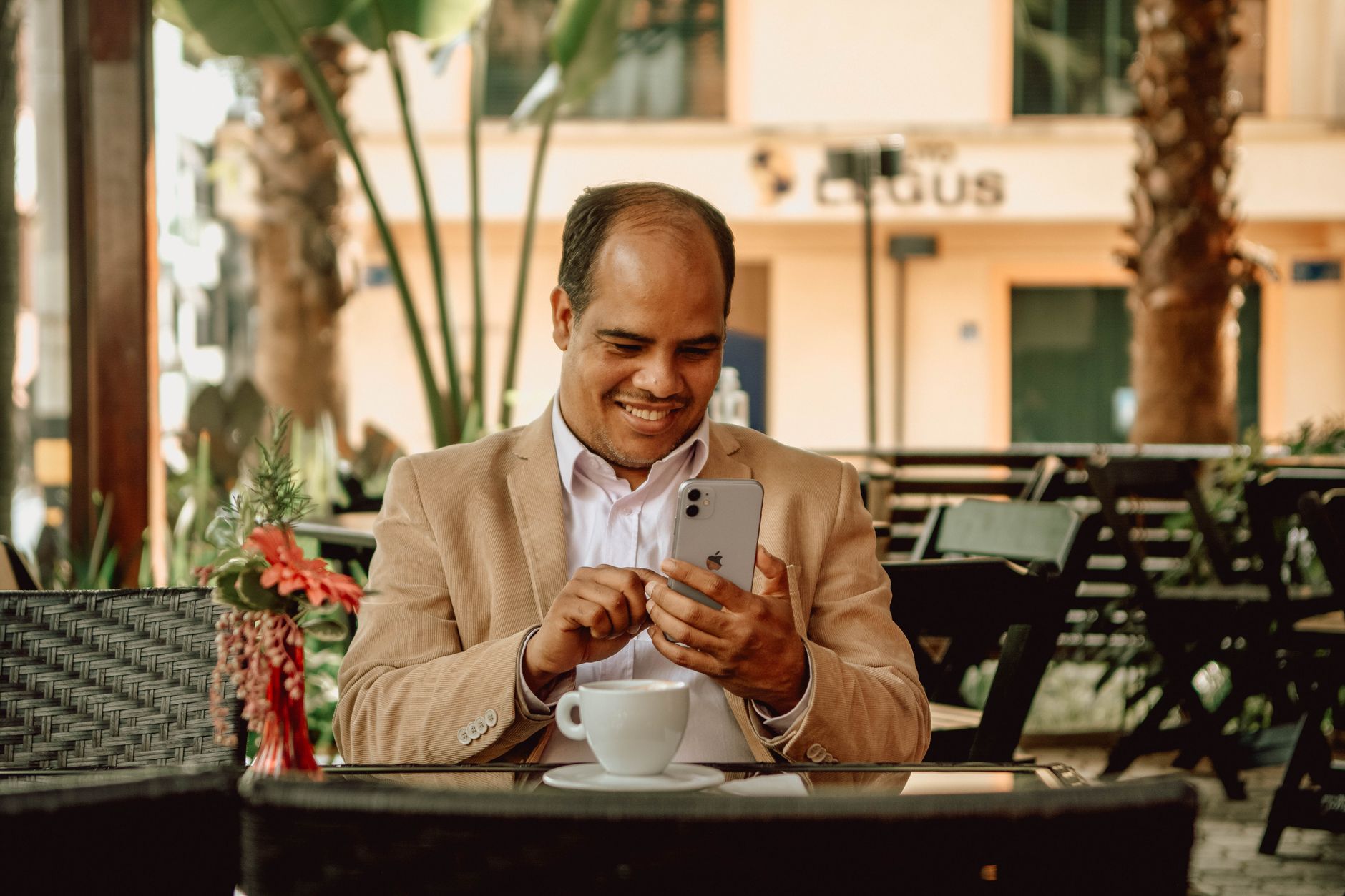 Homem sorrindo enquanto usa o celular em um café