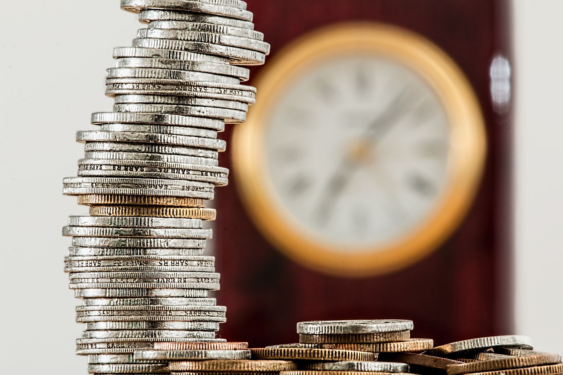 Pilha de moedas ao lado de um relógio de mesa