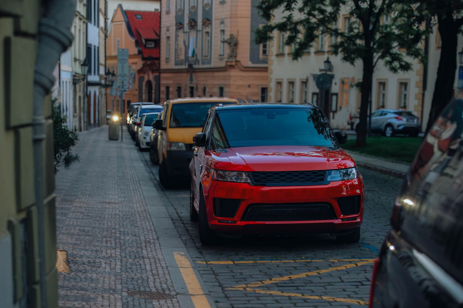 Carro vermelho estacionado em uma rua estreita de paralelepípedos