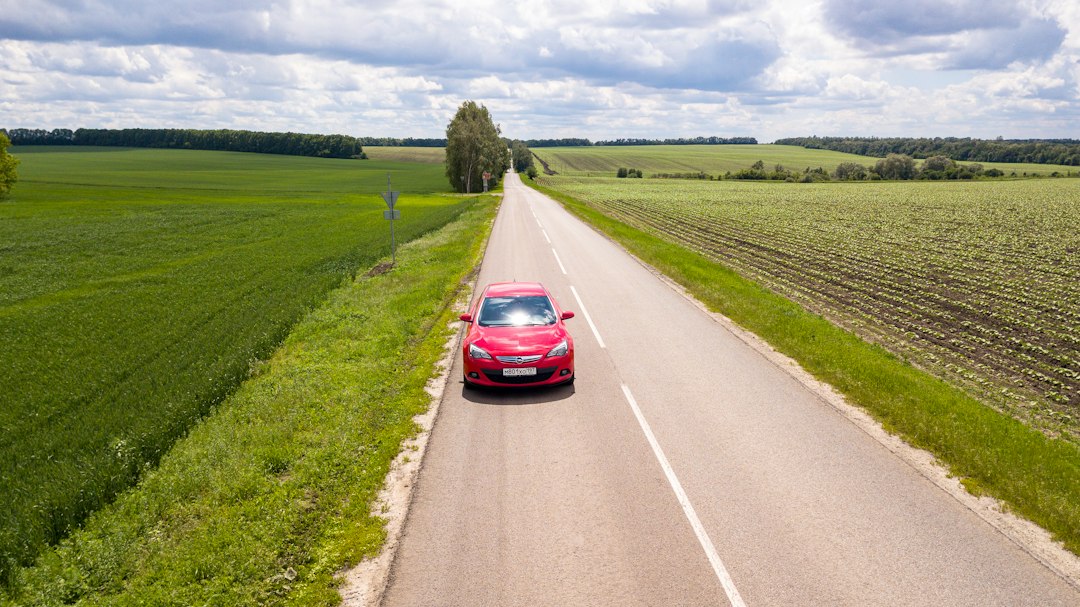 Carro vermelho em uma estrada rural entre campos verdes