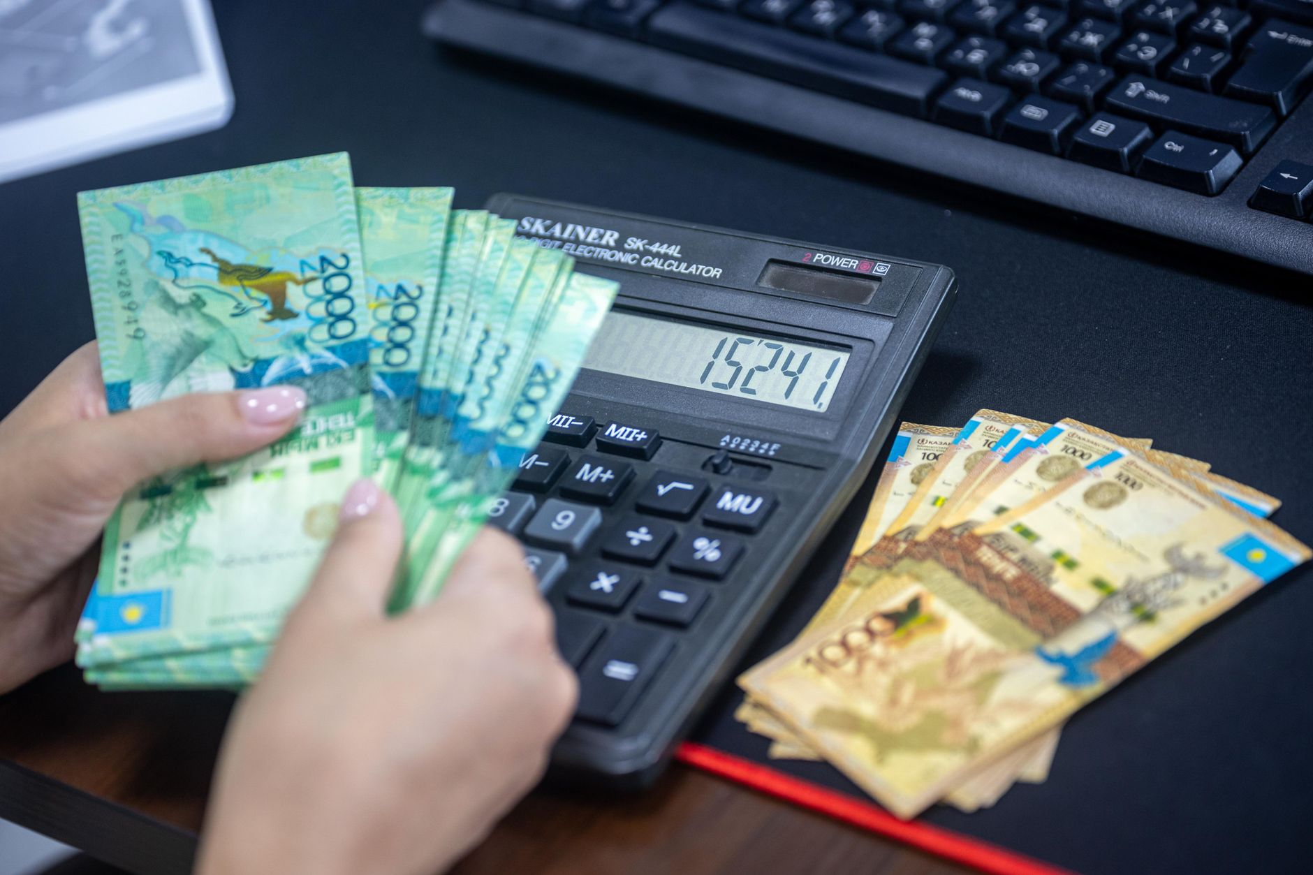 Mãos contando notas ao lado de uma calculadora